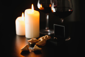 Romantic composition: glasses of wine, burning candles, a box with a wedding ring and cookies with...