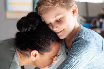smiling young mom and little preschooler son embrace look at camera posing at home