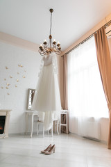 bright room of the bride, a wedding dress hanging on the floor of the chandelier shoes
