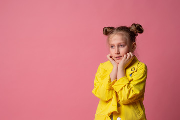 handsome girl with two tails hairstyle hand touching face looking at empty space in yellow jacket on pink background
