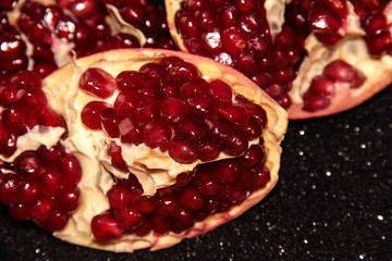 Juicy pomegranate on a black shiny background. Bright pomegranate berries.