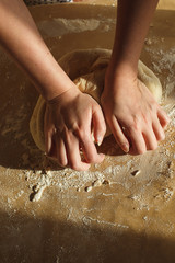 Woman's hands knead dough on a table in warm sunlight. Vertical closeup image.