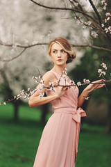 young stylish woman near blossoming flowering tree in the park. spring background. blonde girl with...