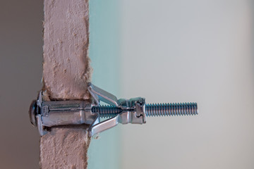 Metal Molly fastener fixed in a pre-drilled hole in a sheet of moisture-resistant drywall, split...