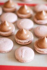 Brown macaroons with chocolate ganache on silicone mat. Cooking process. Selective focus.