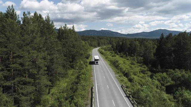 Wagon driving on the highway surrounded by green trees, aerial view. Scene. Transport, logistics concept, white truck driving on the empty road along green forest.