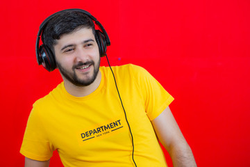 Joyful guy in headphones smiling looking to the side and standing on red background