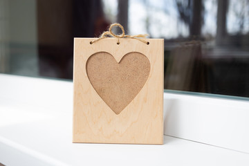 A wooden heart-shaped photo frame stands on the windowsill. Eco present for lovers. Memory souvenir.