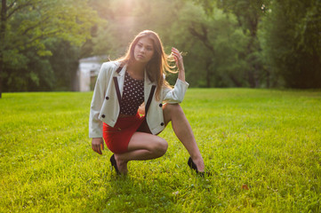 Fototapeta premium Beautiful and attractive girl is relaxing in the park on a summer day. Dressed and posing like a professional model with glasses and a red skirt
