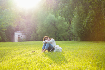 Fototapeta na wymiar Beautiful girl sits on a meadow with grass in the sunlight. Her mood is joyful, happy, sad and tender. Femininity in all gestures. Happy woman's day. Summer