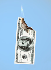 Burning hundred dollars cash on blue background