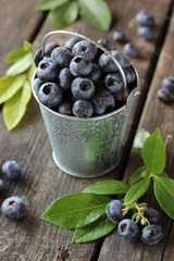 Harvest, gardening. Blueberries in a bucket with leaves and with drops of water on an old wooden background. Summer. Berries in the country. Rustic. Background image, copy space