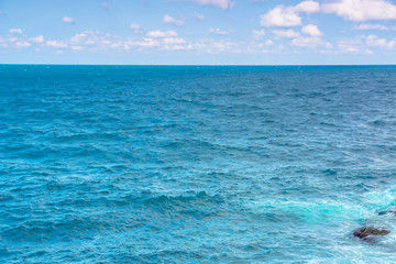 Fototapeta premium rocky sea shore in the afternoon. blue waves crashing the coast. fluffy clouds above the horizon.