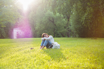 Naklejka na ściany i meble Beautiful girl sits on a meadow with grass in the sunlight. Her mood is joyful, happy, sad and tender. Femininity in all gestures. Happy woman's day. Summer