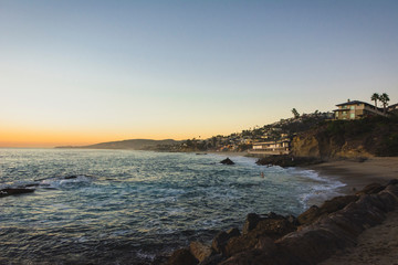 Atardecer en Laguna Beach, California. Vista de paraíso con atardecer iluminando la playa, olas, orilla, mar, arena, casas y palmeras. 