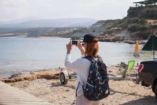 Young woman traveler on the shore of a beach takes pictures on smartphone