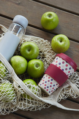An eco bag with bottle of water, eco coffee cup, green apples