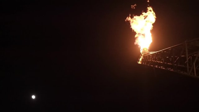 Oil and gas. A slow motion view gas flare tip from bottom burning at oil and gas platform at night with dark sky.