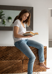 Young woman sitting and reading a book at home