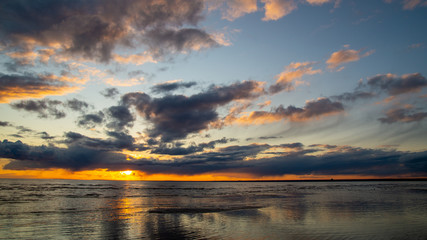 Fototapeta premium Beautiful clouds in the sunset rays on the sandy beach of the sea.