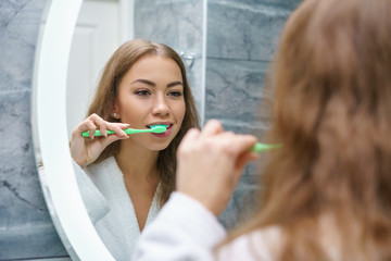 A beautiful young woman brushes her teeth and looks in the mirror