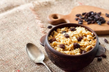 Sweet millet porridge with dark raisins in ceramic rustic bowl
