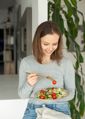 Young woman having healthy lunch at home eating vegetable salad
