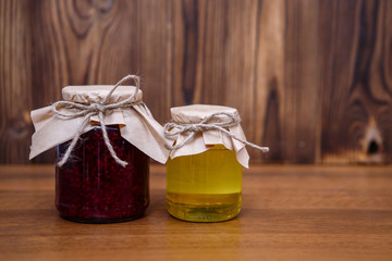 Raspberry jam and honey in glass jars on a wooden background, space for text. A useful remedy for colds.