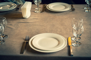 The served table in the restaurant. Clean dishes and appliances on the tablecloth in a cafe. Shiny transparent glasses. White plates. Prepared for the reception of guests. High service.