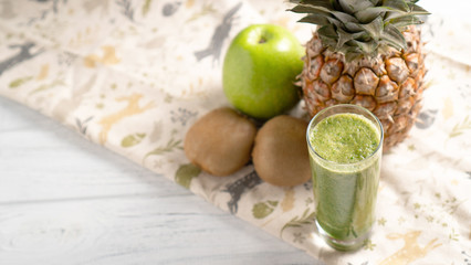 Protect your heart. Green kiwi apple pineapple smoothie in the glass with fruits on background with space for text.