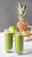 Apple pineapple kiwi smoothie on gray background with fruits behind. Refreshing green superpower summer drink. Vertical