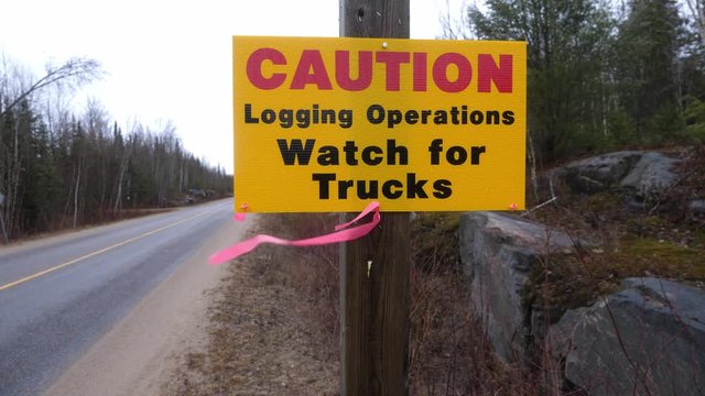 Medium shot of roadside sign that reads, "Caution Logging Operations. Watch for Trucks." Haliburton, Ontario, Canada.