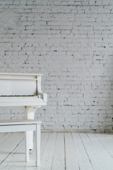 A white piano on a white brick wall. Copy space. Minimalism. Vertical photo