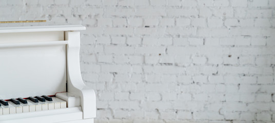 A white piano on a white brick wall. Copy space. Minimalism. Wide horizontal photo