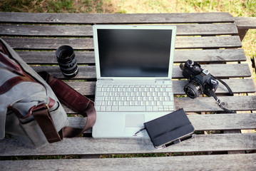 composition on wooden table with vintage camera, notebook, laptop and camera bag. Concept being productivity of photojournalist or photographer - obrazy, fototapety, plakaty