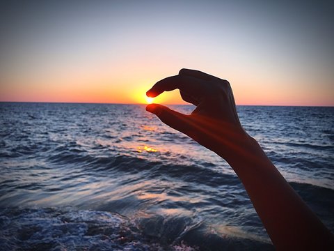 Optical Illusion Of Hand Holding Sun During Sunset