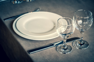 The served table in the restaurant. Clean dishes and appliances on the tablecloth in a cafe. Shiny transparent glasses. White plates. Prepared for the reception of guests. High service.