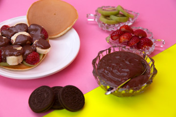 Chocolate poured fruit cake and pancakes. pink-green background.