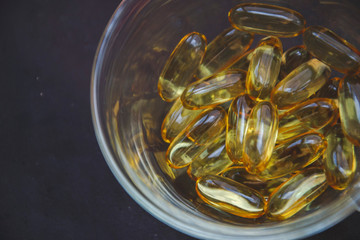 Close up picture of omega 3 in sheer glass bowl on dark background. Fish oil in vitamin pills. Dark background with medical care for people. Pharmacy flat lay wallpaper. Copy space of medicament care.
