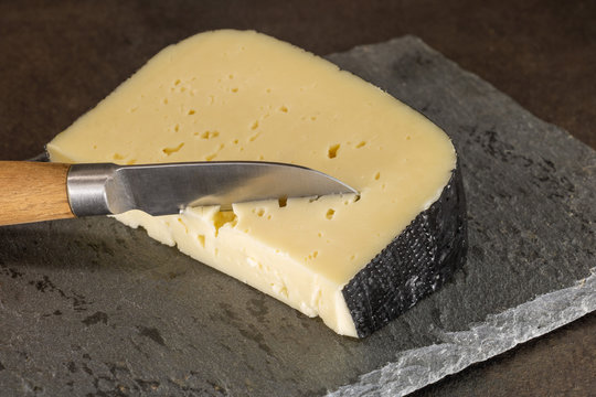 morceau de tomme des Pyrénées sur un plateau de service en ardoise avec un couteau planté dans le fromage