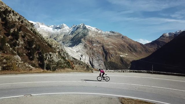 Professional road cyclist ride on carbon bicycle up curve on narrow swiss mountain road. Legendary Furka pass in distance. Cycling inspiration and epic destination for athletic goals