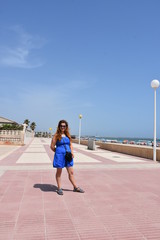 Girl in a blue dress stands on the beach