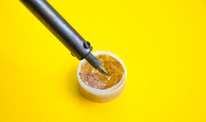 Soldering iron, tin, rosin on a yellow background. Soldering iron in male hands. Macro. Repair of electrical equipment, radio engineering. Solder wires, contacts.  Copy Space