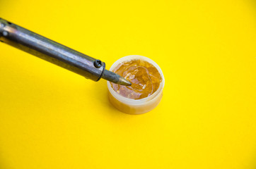 Soldering iron, tin, rosin on a yellow background. Soldering iron in male hands. Macro. Repair of electrical equipment, radio engineering. Solder wires, contacts.  Copy Space