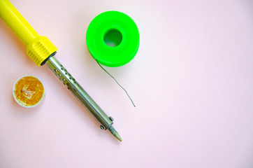 Soldering iron, tin, rosin on a pink background. Soldering iron in male hands. Macro. Repair of electrical equipment, radio engineering. Solder wires, contacts.  Copy Space