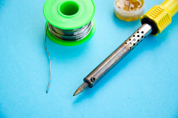 Soldering iron, tin, rosin on a blue background. Soldering iron in male hands. Macro. Repair of...