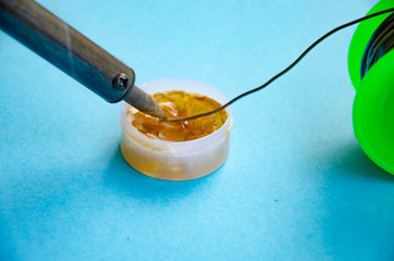 Soldering iron, tin, rosin on a blue background. Soldering iron in male hands. Macro. Repair of electrical equipment, radio engineering. Solder wires, contacts.  Copy Space