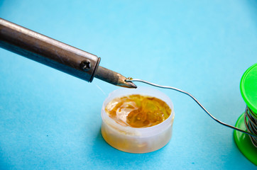 Soldering iron, tin, rosin on a blue background. Soldering iron in male hands. Macro. Repair of electrical equipment, radio engineering. Solder wires, contacts.  Copy Space