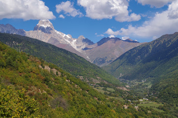 Fototapeta premium Scenic autumn landscape in the mountains of the Caucasus. View of the valley and village on the background of snowcapped peak of the Ushba Mountain. Nature and travel. Georgia, Svaneti region