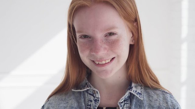 Funny redhead teenage girl with freckles against white wall with sun rays
